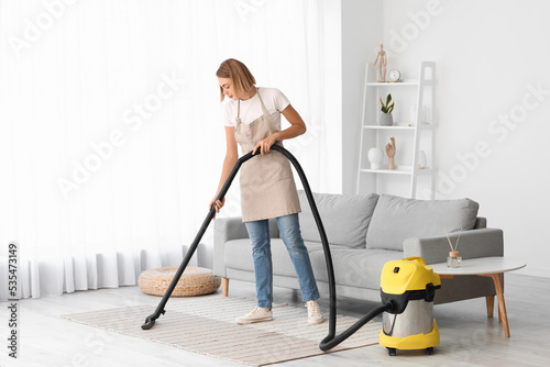 Young housewife cleaning carpet with vacuum cleaner at home