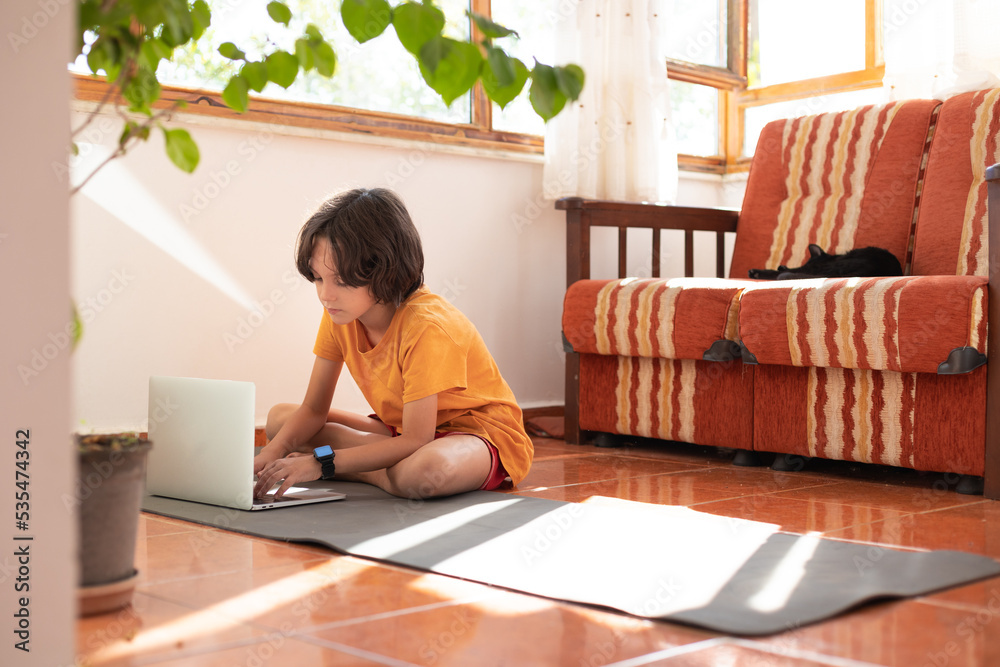 Distance learning. The boy sits on the floor at home and works on a laptop. Children use technology