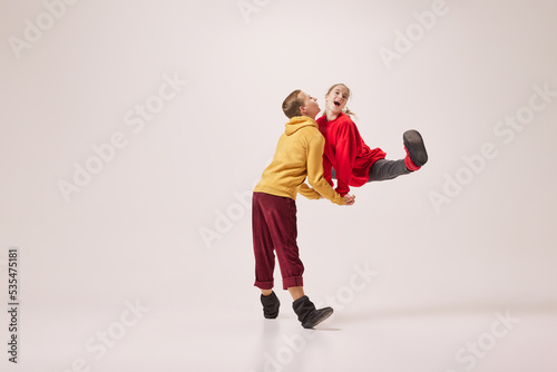Emotional flexible young couple of ballet dancers in warm winter homewear dancing isolated on grey background. Retro, vintage, dance, holidays, party concept