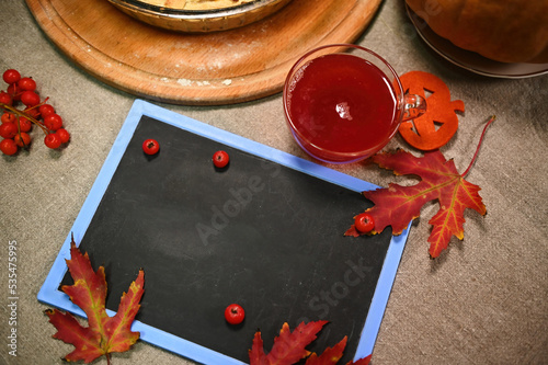 Top view of a blank chalk board with copy advertising space for a promotional text, ripe red viburnum berries, red maple autumn leaves and a glass cup of hot mulled wine on the linen tableclot photo