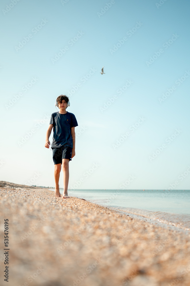 Teenager 13 years old listen to music on the beach by the sea
