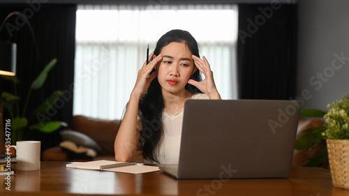 Tired asian woman entrepreneur holding her head in hands, exhausted from overwork or stress at work