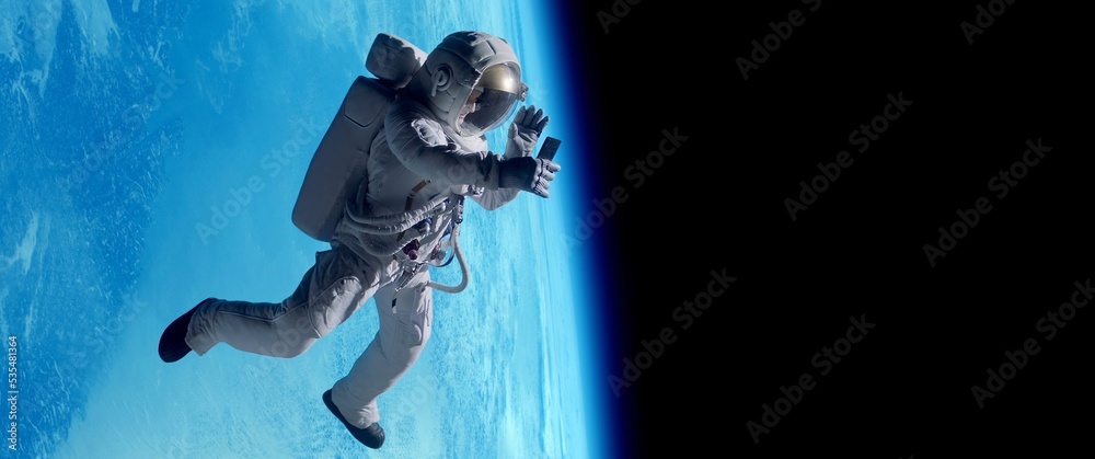 Fototapeta premium Female astronaut having a video call on her phone while performing space walk in open space, Earth in the background