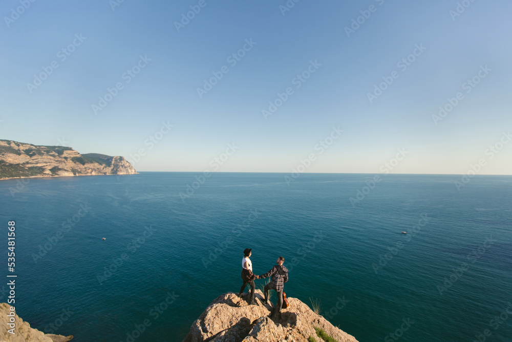 Couple in love on a mountaintop overlooking the sea. Man plays the guitar, a woman in a hat sings.