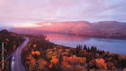 Aerial view of a lake surrounded by trees and hills near a highway in the Dalles, Oregon at sunset