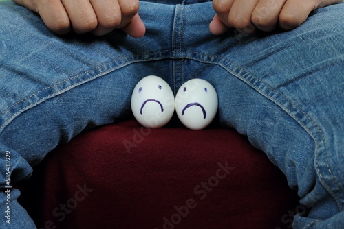 Young Asian man holding two chicken eggs with sad face on crotch groin area. Male infertility, testicular cancer and impotence concept.  photo