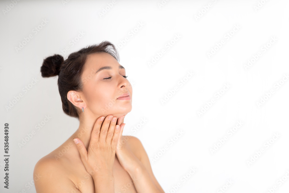 A young beautiful brunette woman massages her face and neck. The naturalness of self-care. White background place for text A young beautiful brunette woman massages her face and neck. The naturalness of self-care. White background place for text