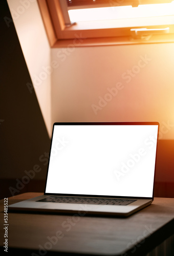 A new professional laptop is on the wooden table. Design template for application or website. Mock-up of a notebook with a blank screen in the modern house interior. Silver aluminum laptop.
