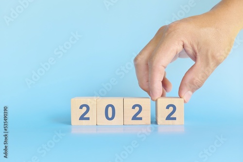 Year 2022 end, conclude and finalize concept. Human hand completing wooden blocks in blue background. 