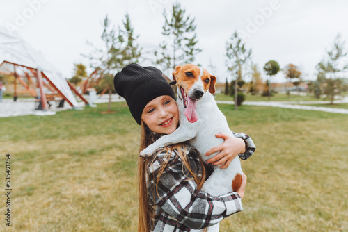 a little girl kisses and hugs her Jack Russell terrier dog in the park. Love between the owner and the dog. a child is holding a dog in his arms. © inna717