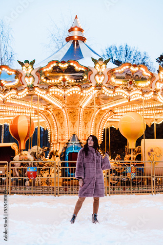 A girl in a fur coat near a beautiful French merry-go-round Snow winter