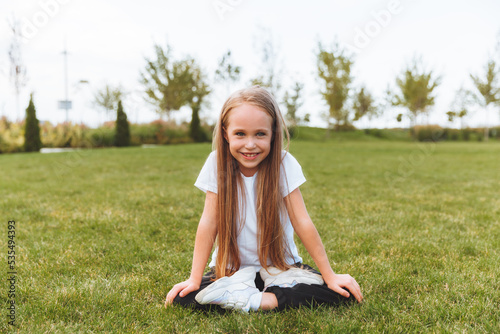 A sweet, happy little girl sitting on the grass in the park. Laughing, enjoying the fresh air.the child is sitting on the grass