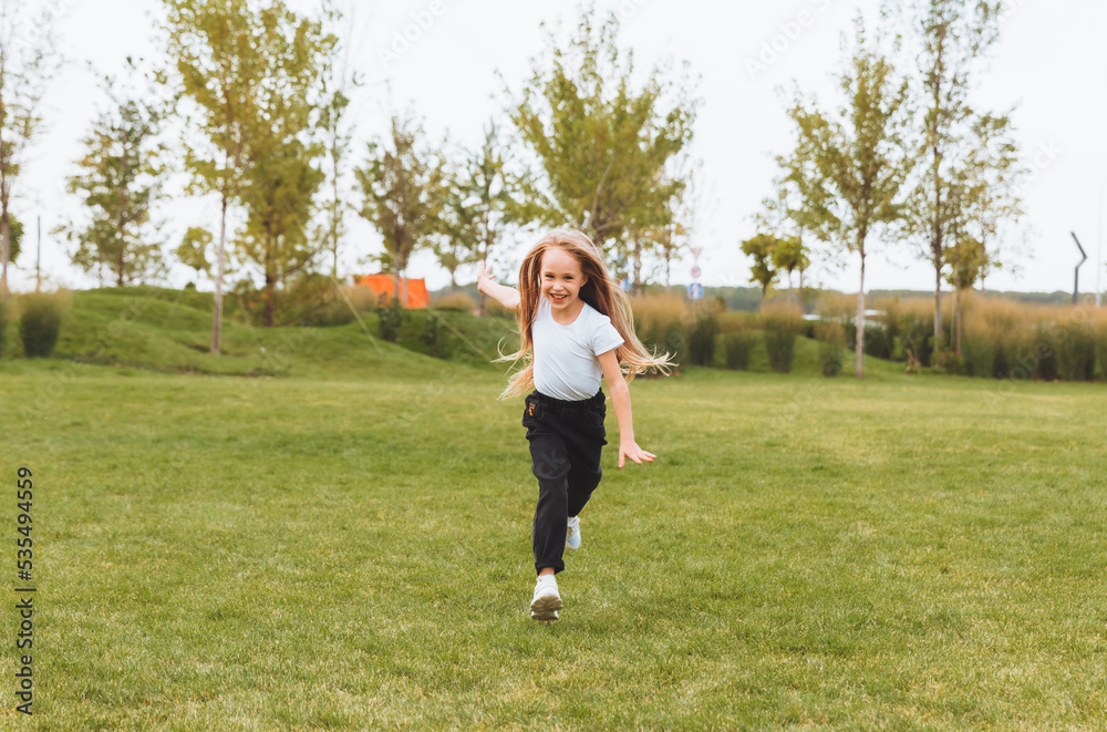 a little cheerful girl with long hair runs through the grass in the park and rejoices. a little cheerful girl with long hair runs through the grass in the park and rejoices.