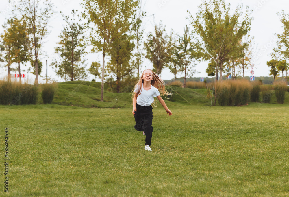 a little cheerful girl with long hair runs through the grass in the park and rejoices.