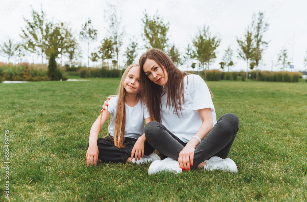 A happy mother and her daughter are sitting on the grass in the park and hugging. mother and daughter. family.joyful mom and little girl A happy mother and her daughter are sitting on the grass in the park and hugging. mother and daughter. family.joyful mom and little girl