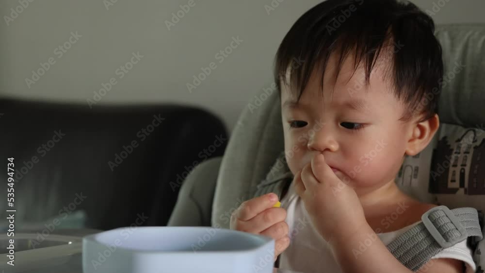 Joyful Asian Chinese baby boy holding food with dirty face during having lunch Joyful Asian Chinese baby boy holding food with dirty face during having lunch