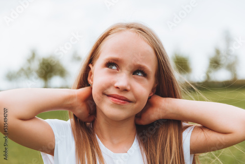 Charming happy little girl with blonde hair outdoors in the park. Portrait of a Caucasian child enjoying the sun.