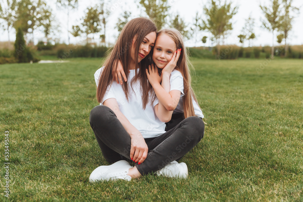 A happy mother and her daughter are sitting on the grass in the park and hugging. mother and daughter. family.joyful mom and little girl A happy mother and her daughter are sitting on the grass in the park and hugging. mother and daughter. family.joyful mom and little girl