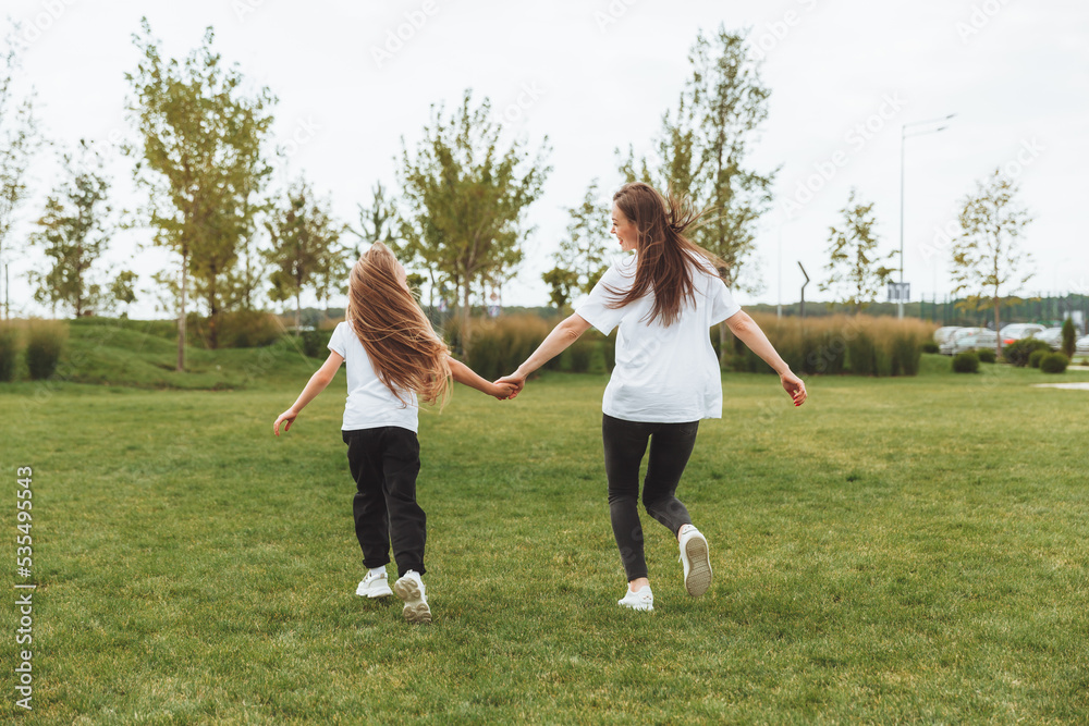 Mother and daughter play and run around the park on a beautiful day. the family is having fun in the park on the grass. morning jog. Mother and daughter play and run around the park on a beautiful day. the family is having fun in the park on the grass. morning jog.