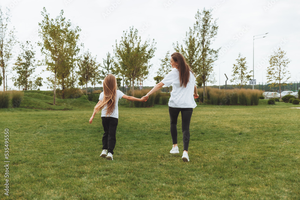 Mother and daughter play and run around the park on a beautiful day. the family is having fun in the park on the grass. morning jog.