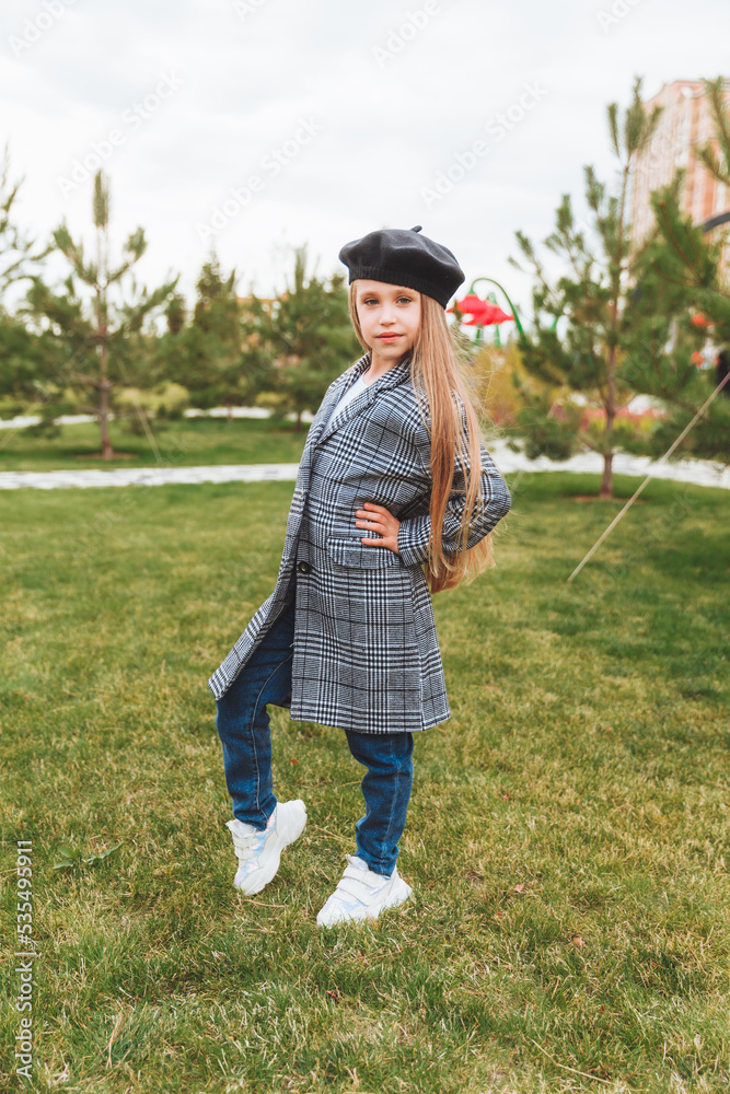 A beautiful smiling little girl with blue eyes in an autumn coat and beret poses in the park.