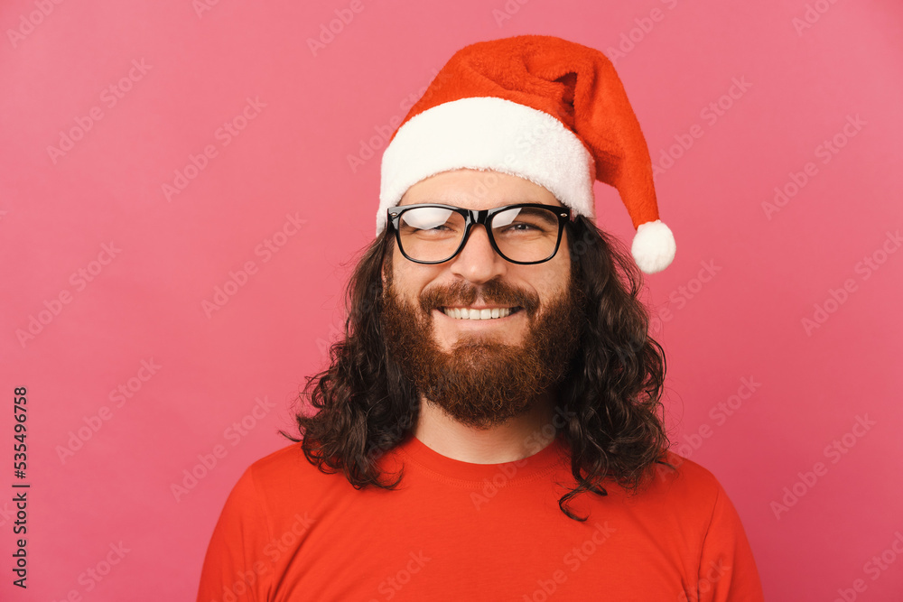 Portrait of young bearde man wearing glasses and santa claus hat over pink background. Portrait of young bearde man wearing glasses and santa claus hat over pink background.
