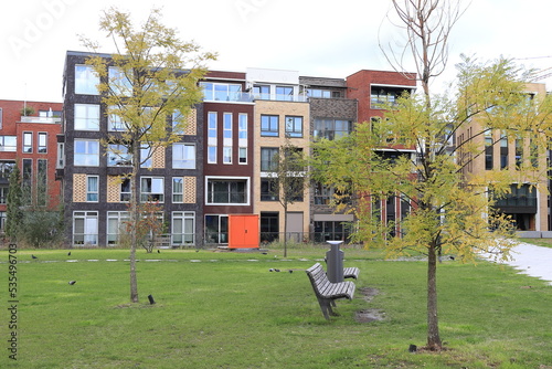 Amsterdam Memeleiland Modern Residential Buildings with Grass Field, Autumn Trees, Bench and Orange Container, Netherlands © Monica