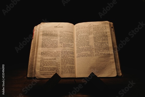 Closeup shot of a historic old Bible open on the Obadiah pages on display in a dark room photo