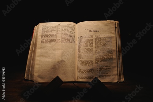 Closeup shot of a historic old Bible open on the Romans pages on display in a dark room