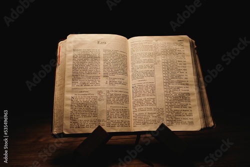Fotomural Closeup shot of a historic old Bible open on the Ezra pages on display in a dark