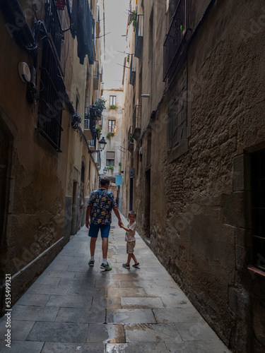father and son stroll hand in hand down a narrow street © Quiles