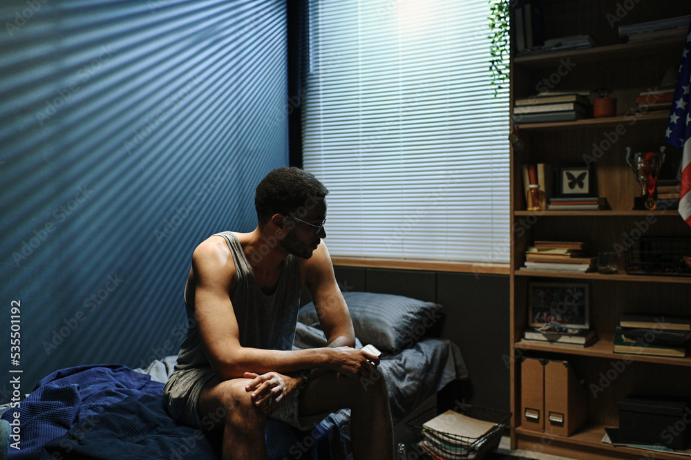 Young sleepless man in underwear and eyeglasses sitting on bed at midnight and suffering from post traumatic syndrome Young sleepless man in underwear and eyeglasses sitting on bed at midnight and suffering from post traumatic syndrome