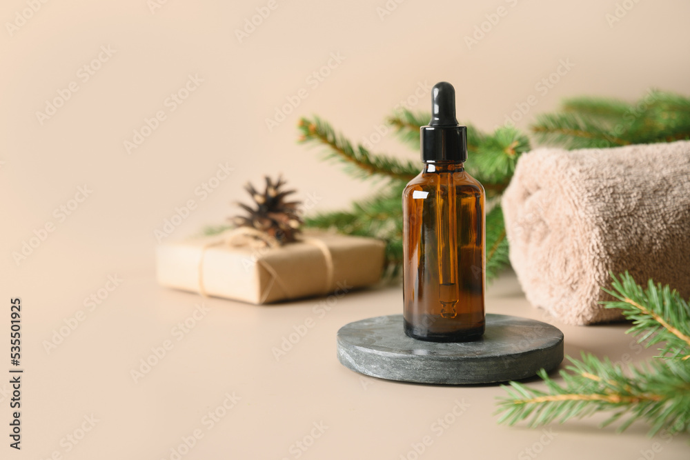 Naklejka premium Christmas Spa concept with cosmetic aroma oil, pine cones, evergreen branches on beige background. Winter holiday for body care and wellness. Vertical format. Close up.