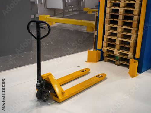 Hand pallet truck. Hydraulic pallet truck on background of warehouse interior. Yellow manual forklift. Old hand pallet truck with no one. Manual storage equipment. Storehouse transportation machine