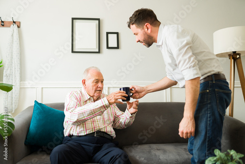 Fotografia Young son bringing coffee while chatting with his old senior father