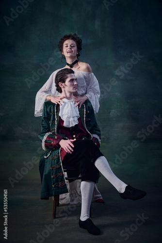 Portrait of legend medieval lady, woman in image of vampire strangling young man over dark green background. Victim