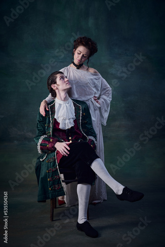 Portrait of beautiful woman with pale skin standing near young boy over dark green background. Vampire lady