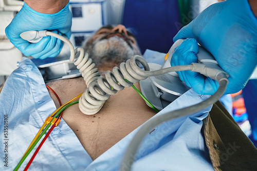 Ambulance worker using portable defibrillator in attempt to revive senior man inside ambulance who has suffered heart attack. Defibrillator pads in paramedic hands, close-up