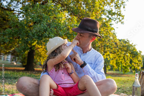 Father and little daughter sitting on the mat in the park play touching each other's noses © Media Lens King