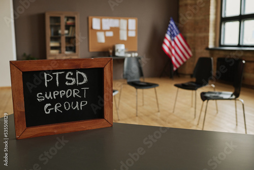 Small chalkboard with notice about PTSD support group on table standing against circle of several chairs for attendants in studio