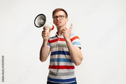 Portrait of young man in glasses posing with megaphone isolated over white studio background. Important news © Lustre