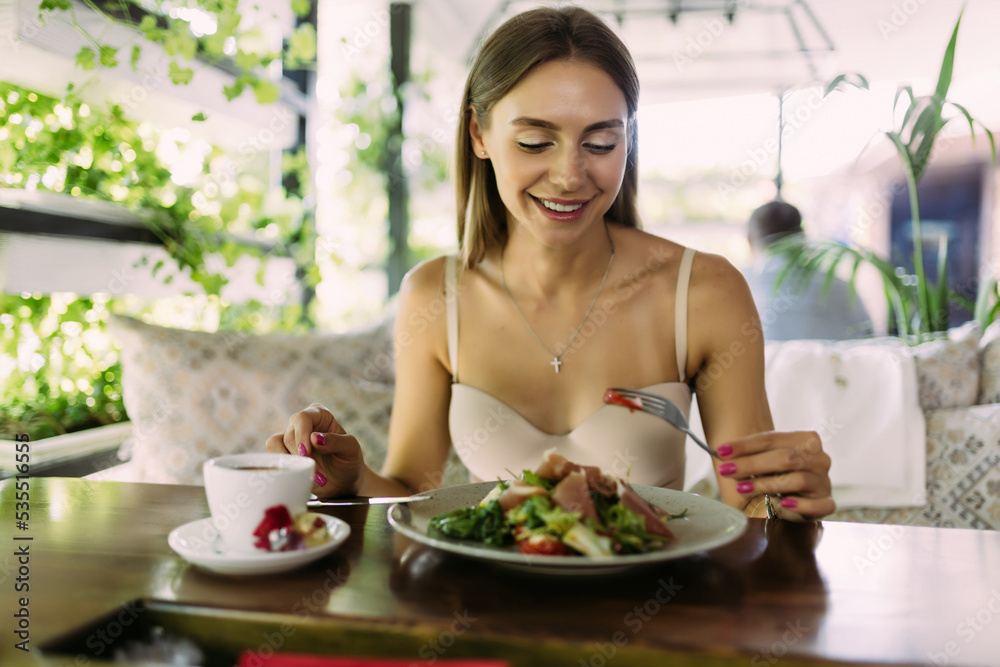 Smiling young woman eating fresh salad in restaurant