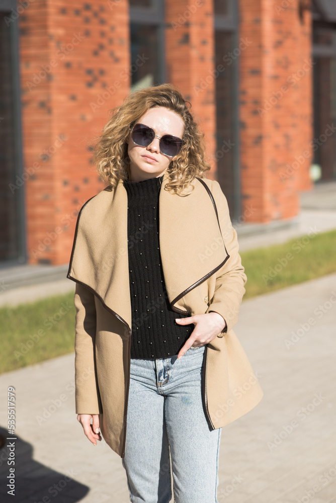 Fototapeta premium Portrait of a young Caucasian girl in a coat and sunglasses in the city on an autumn day.