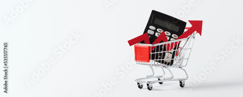 Shopping cart trolley, calculator and red arrow up on white background with copy space. Crisis and rising prices concept