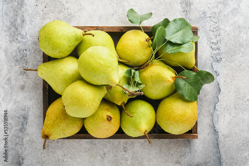 Pears. Fresh sweet organic pears with leaves in wooden box or basket on old gray stone tile background. Autumn harvest of fruits. Top view. Food background.