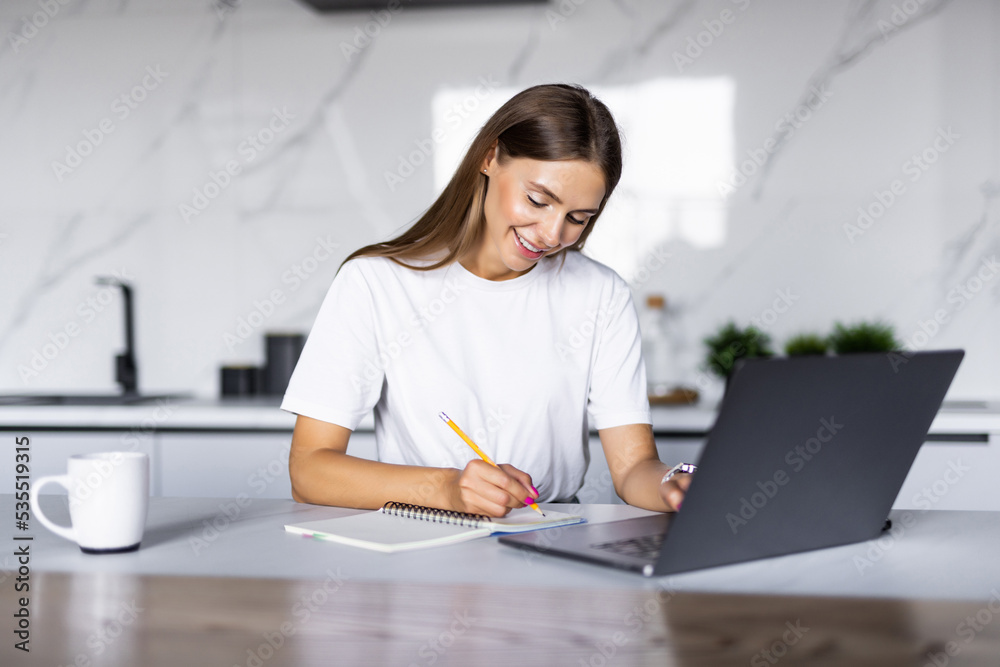 Woman takes notes with pen, using laptop for remote work from home, write down some information sitting at the table. Multitasking concept Woman takes notes with pen, using laptop for remote work from home, write down some information sitting at the table. Multitasking concept