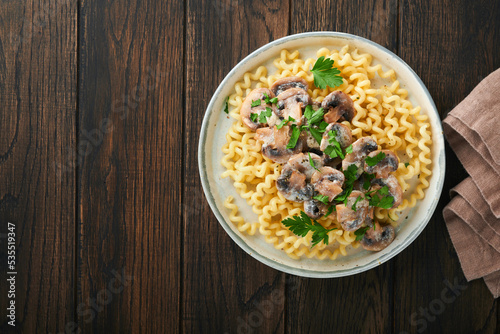 Fusilli pasta with mushrooms, cheese and garlic creamy sauce on plate on old wooden dark table background. Top view. Traditional Italian cuisine.