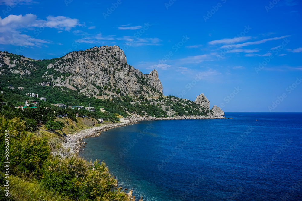 Rock covered with green vegetation hanging over the calm blue sea
