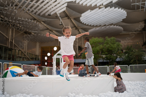 Happy little girl playing white plastic balls pool in amusement park. playground for kids. photo