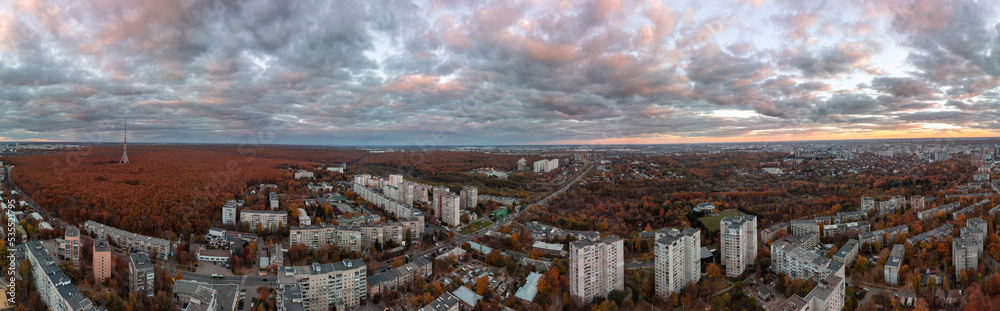 Aerial wide sunset panorama view on autumn city with telecommunication tower in forest near residential district, streets and park. Kharkiv, Ukraine